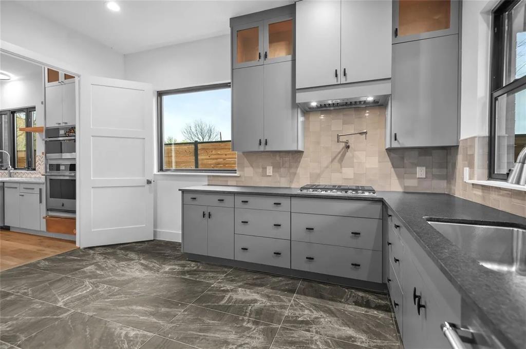 309 Kaye Street Coppell, TX 75019 - Photo 27 of 36 Modern kitchen featuring stone-finish floor tiling, grey cabinetry with dark hardware, dark countertops, and a tiled backsplash