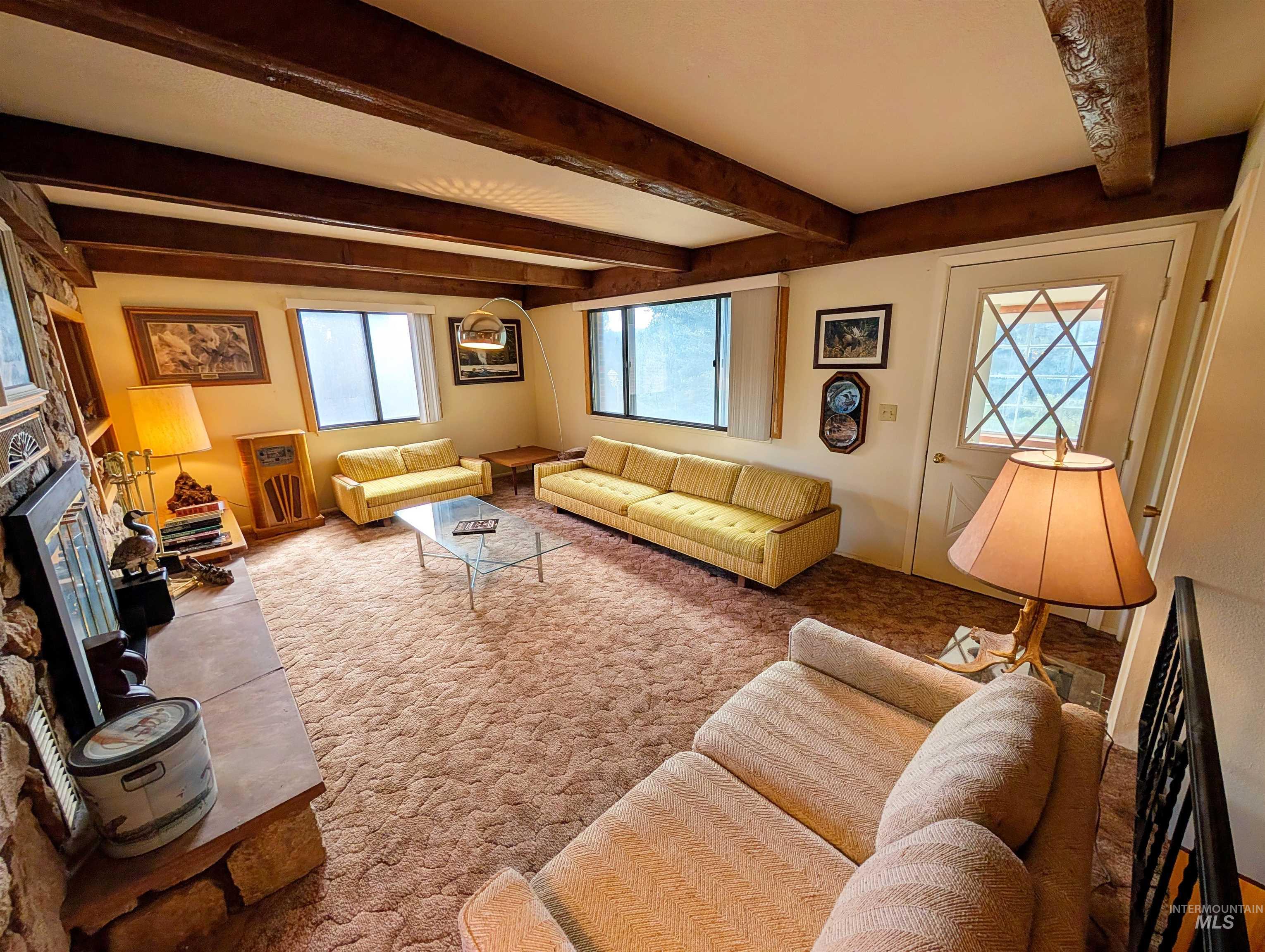 11100 Bens Road Cascade, ID 83611 - Photo 19 of 35 Living area featuring exposed wood ceiling beams, a floor-to-ceiling stone fireplace, multiple windows, and a diamond-pane entryway door