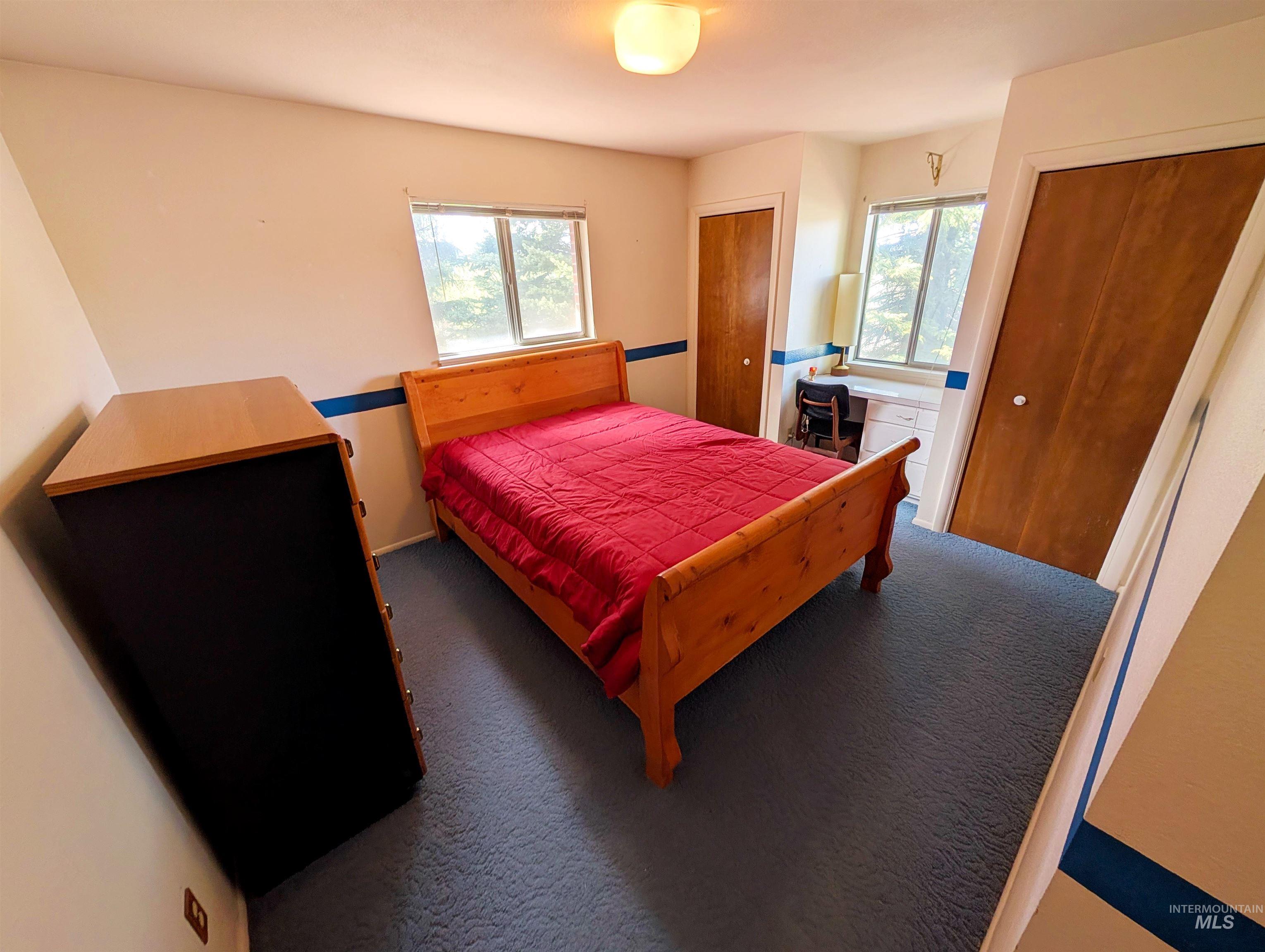 11100 Bens Road Cascade, ID 83611 - Photo 28 of 35 Bedroom featuring two windows, recessed built-in desk, two closet spaces with wood-finish doors, and blue carpeting