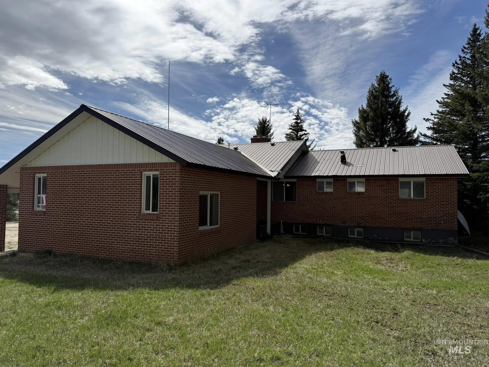 11100 Bens Road Cascade, ID 83611 - Photo 5 of 35 Brick exterior featuring a metal roof, white window frames, and mature trees in the background