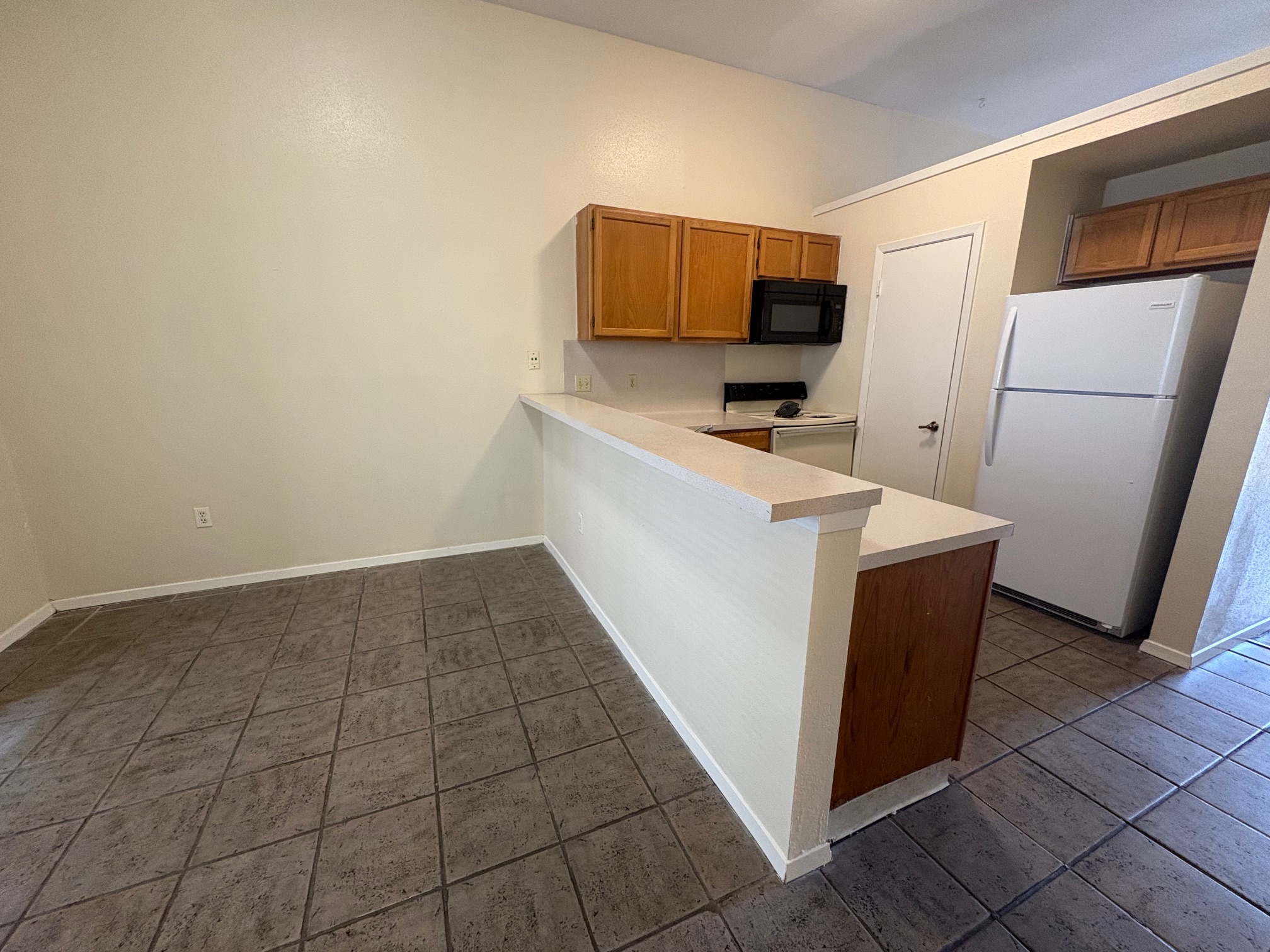 2801 Rio Grande Street, Unit 303 Austin, TX 78705 - Photo 7 of 11 Kitchen with light countertops, brown cabinets, white appliances, a peninsula, and dark tile patterned flooring