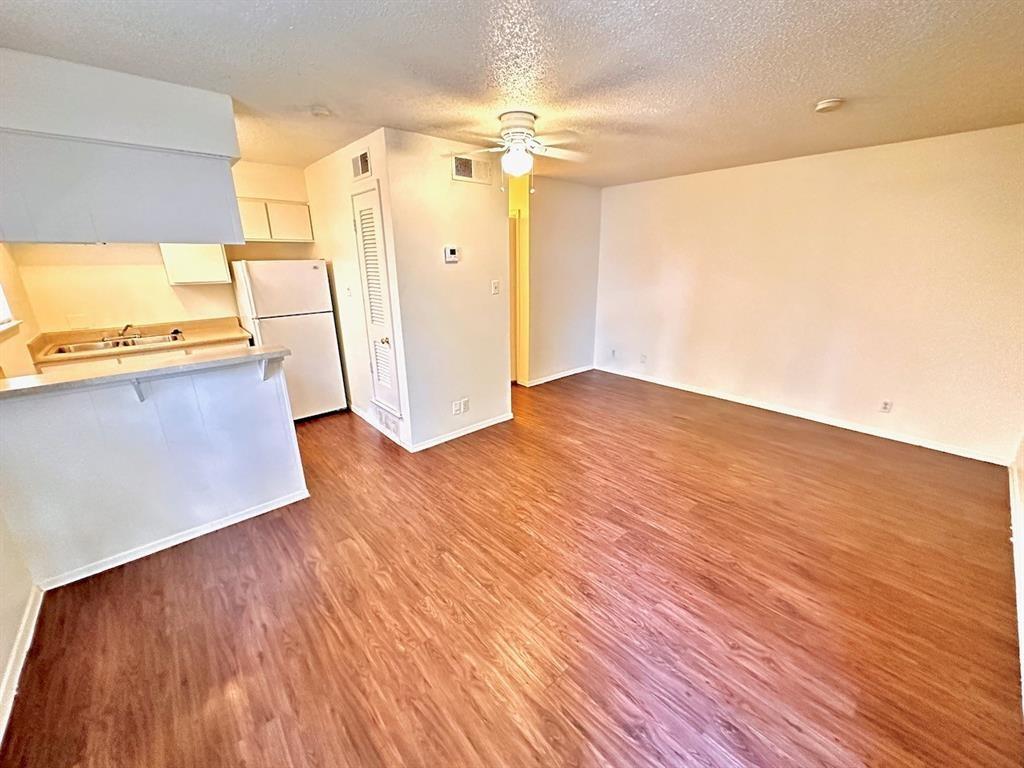 Unfurnished living room with dark wood-style flooring, a textured ceiling, and a ceiling fan
