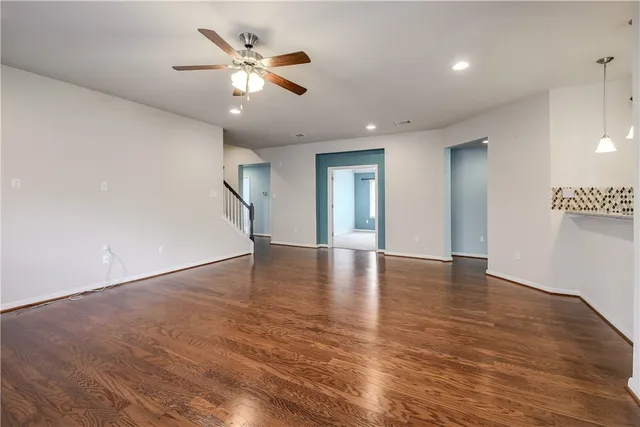 a view of an empty room with wooden floor and a ceiling fan