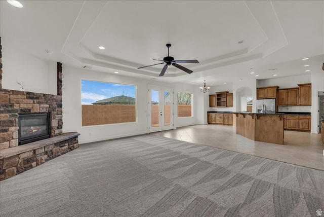 691 Rainier Drive St. George, UT 84770 - Photo 2 of 24 Unfurnished living room featuring light tile patterned floors, hanging lights, ceiling fan, a stone fireplace, and healthy amount of natural light