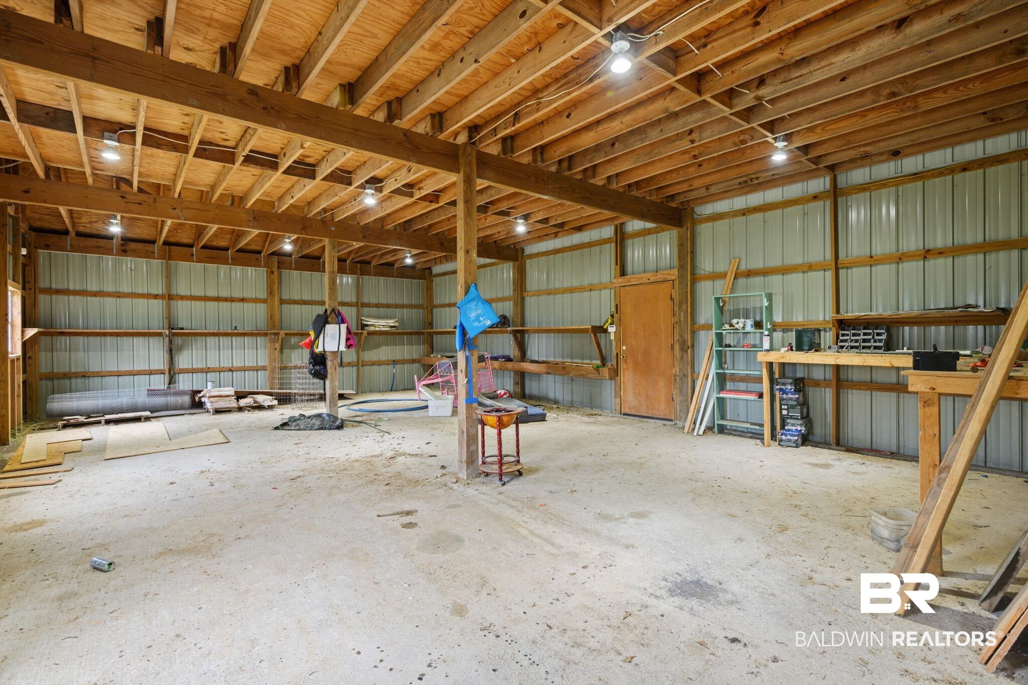 7540 2 Mile Road Irvington, AL 36544 - Photo 61 of 82 Spacious interior structure featuring exposed wood beams, a high wood-finish ceiling, multiple surface-mounted light fixtures, corrugated metal wall panels, and a concrete floor