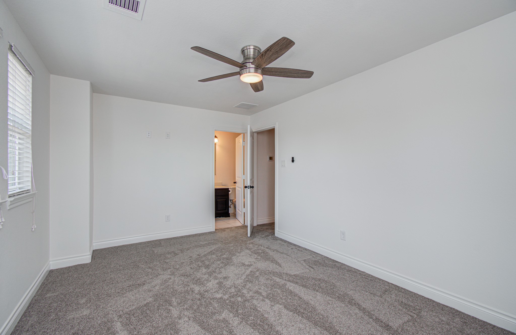6621 North Main Street Houston, TX 77009 - Photo 24 of 41 Third floor secondary bedroom features fresh carpeting, neutral walls, a ceiling fan, and ample natural light from multiple windows. It also has an adjoining bathroom, enhancing convenience and comfort.