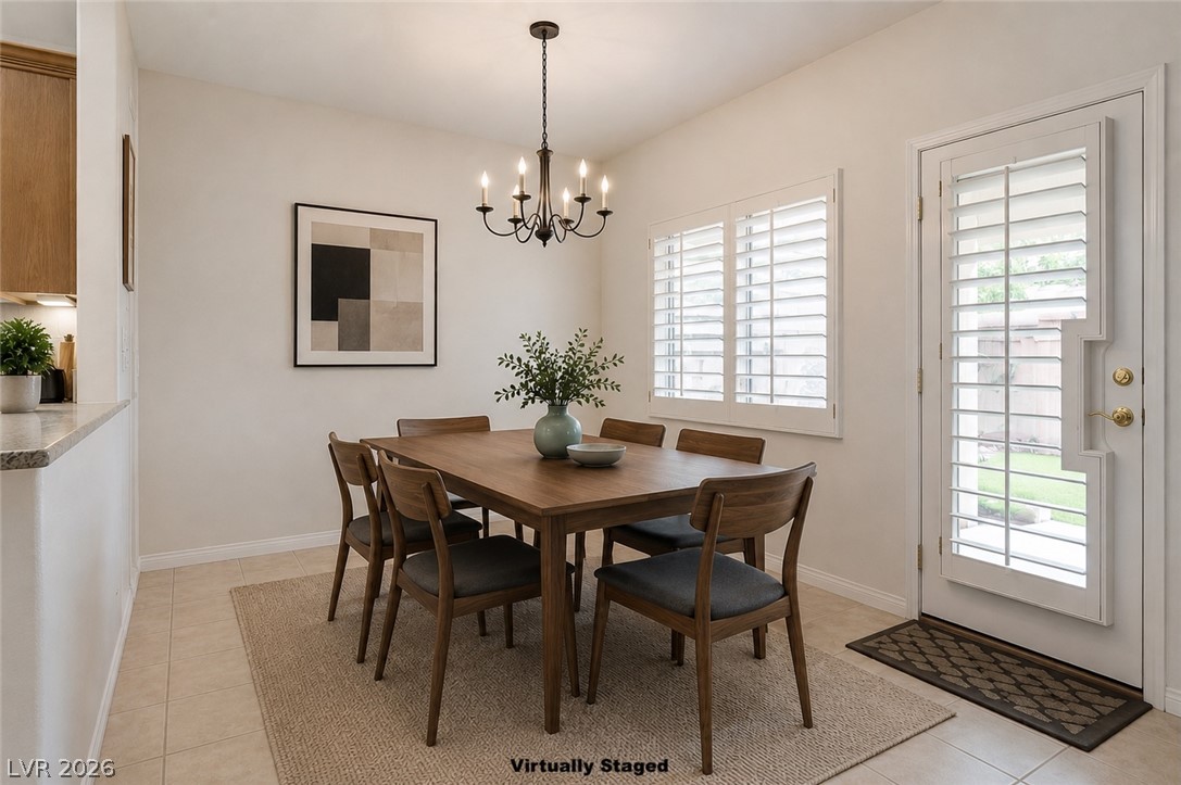1479 Orange Jubilee Road Henderson, NV 89014 - Photo 7 of 36 A well-lit dining area featuring a classic chandelier and direct outdoor access through a door with integrated blinds.