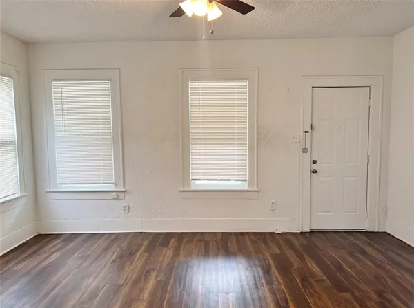 an empty room with wooden floor chandelier fan and windows