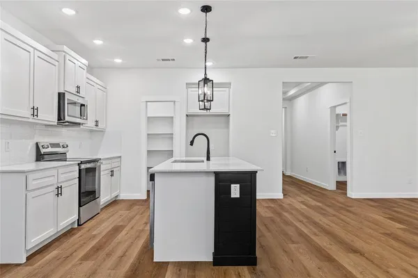 a kitchen with stainless steel appliances granite countertop white cabinets a sink a stove a microwave and wooden floors