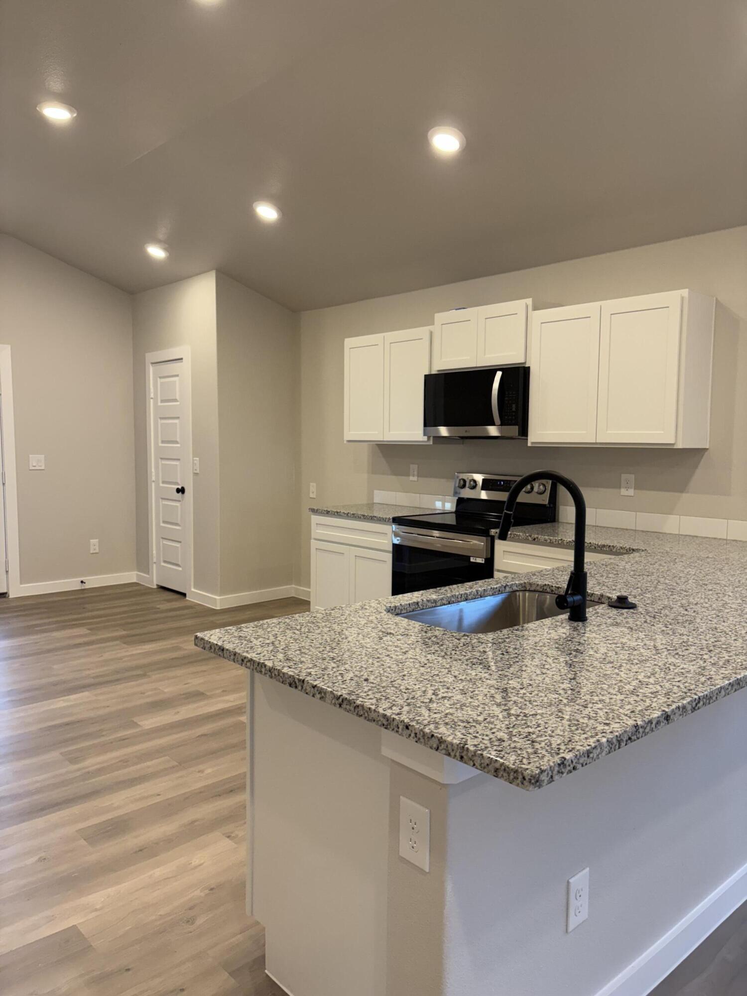 7222 35th Street Lubbock, TX 79407 - Photo 3 of 11 a kitchen with granite countertop a sink and a stove top oven with wooden floor
