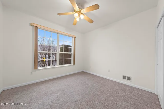 an empty room with chandelier fan and windows