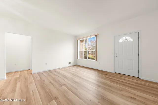 a view of an empty room with wooden floor and a window