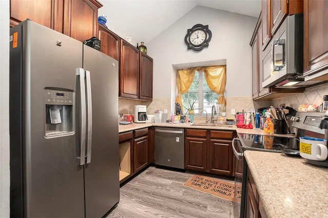 a kitchen with stainless steel appliances granite countertop a refrigerator a sink dishwasher a stove and a dining table with wooden floor