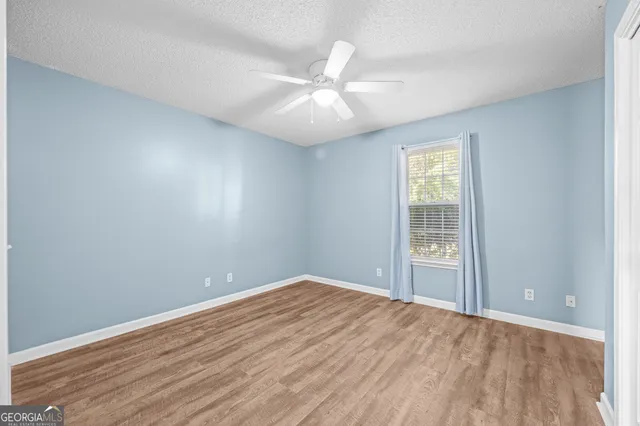 an empty room with wooden floor fan and windows