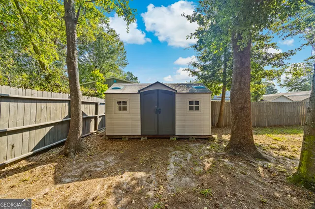 a view of a small house in the backyard with large tree and wooden fence