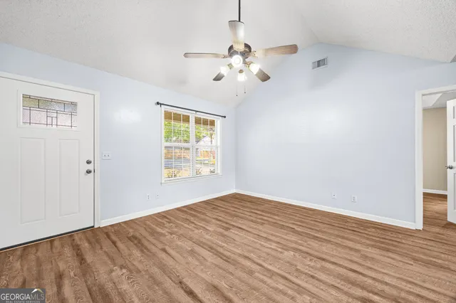 an empty room with wooden floor chandelier fan and windows