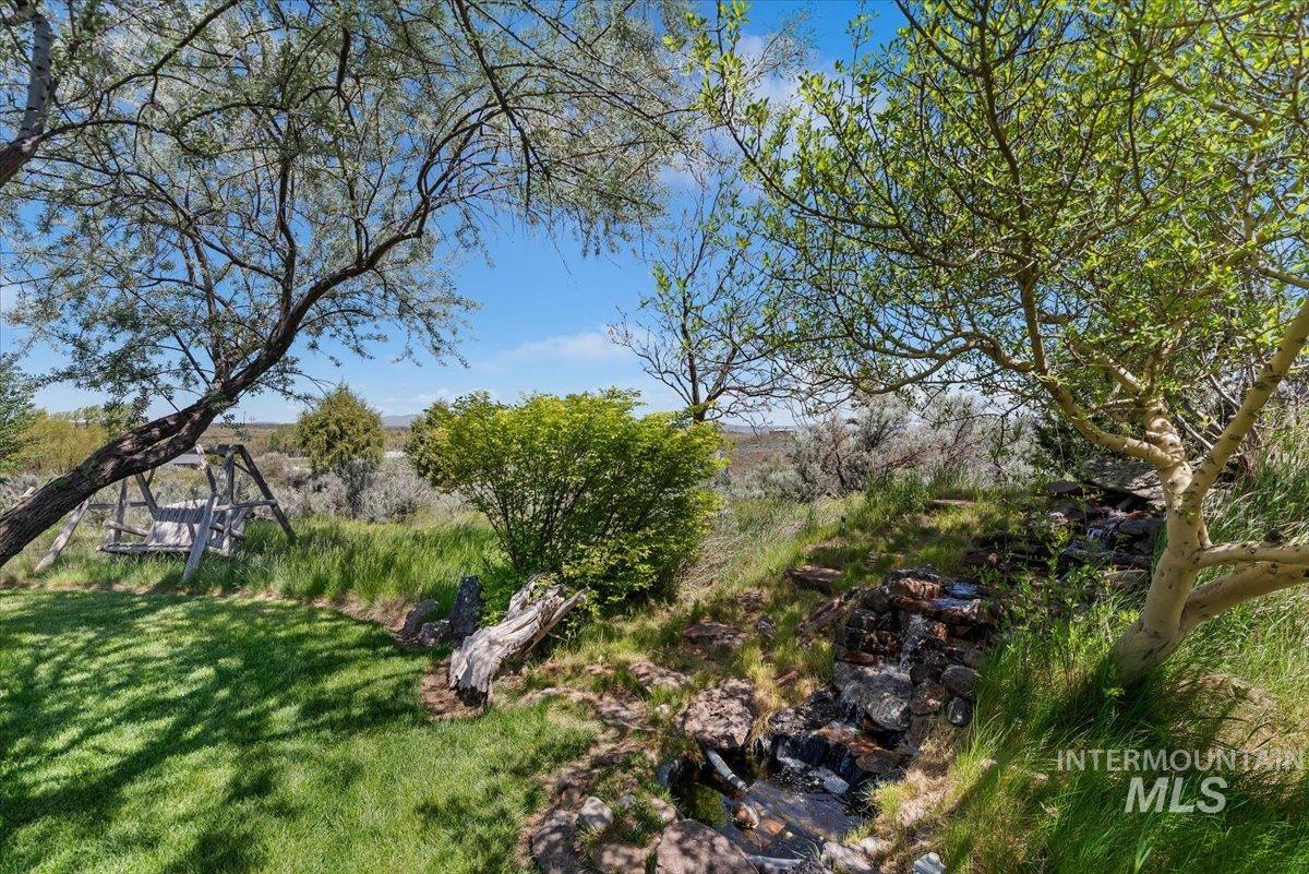 147 East Indian Crk Road Boise, ID 83716 - Photo 38 of 43 Expansive outdoor space featuring a manicured lawn, established trees, a natural rock formation, and mature landscaping