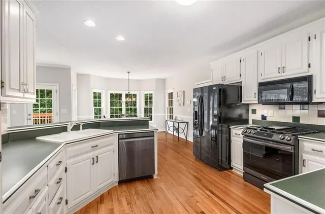 a kitchen with stainless steel appliances white cabinets a sink a stove a refrigerator and wooden floors