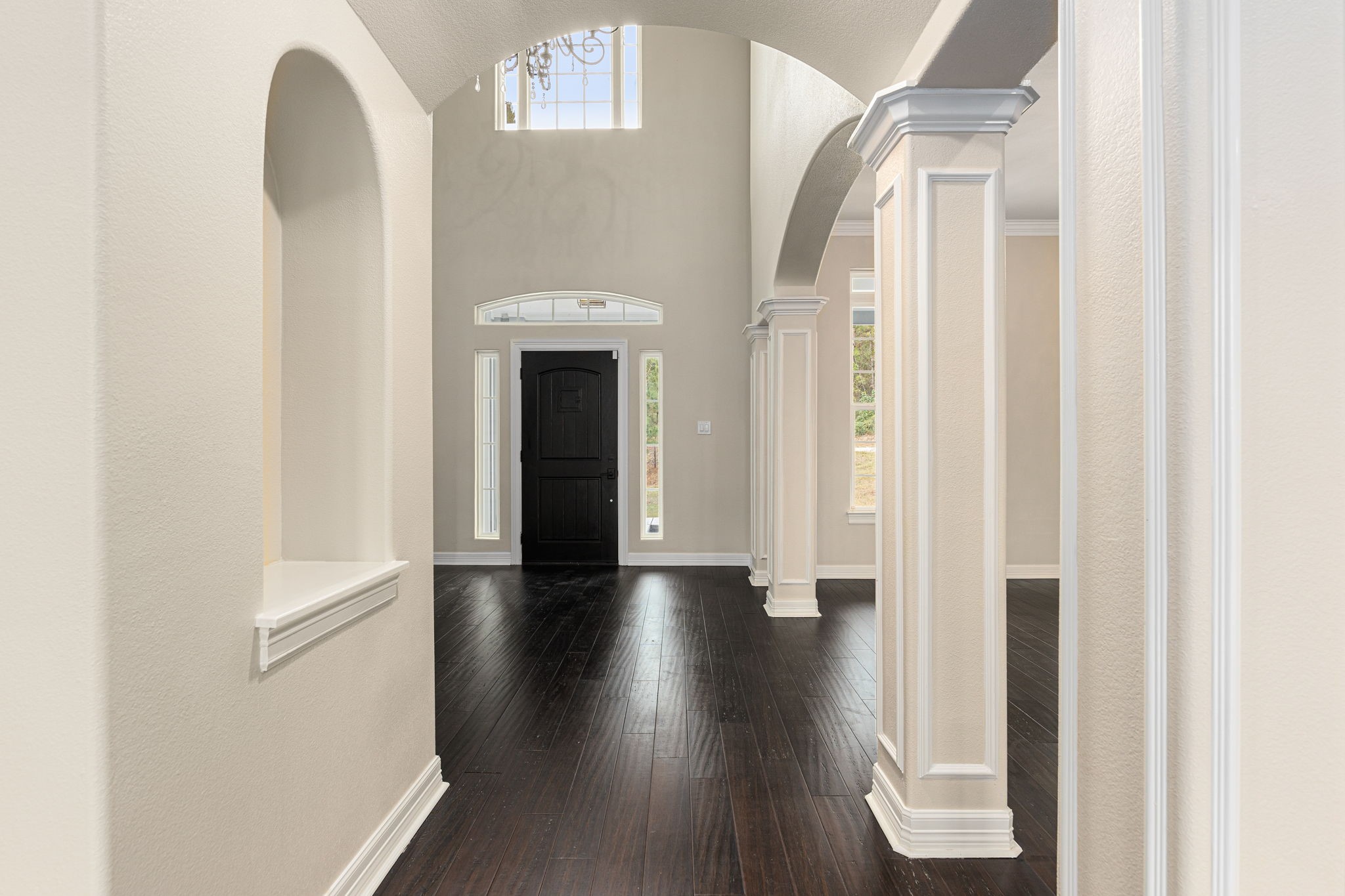 14882 Gingham Road Montgomery, TX 77356 - Photo 9 of 41 This photo showcases a bright, elegant entryway with high ceilings, decorative columns, and dark wood flooring. The arched design and large windows near the door enhance natural light and create a welcoming atmosphere.
