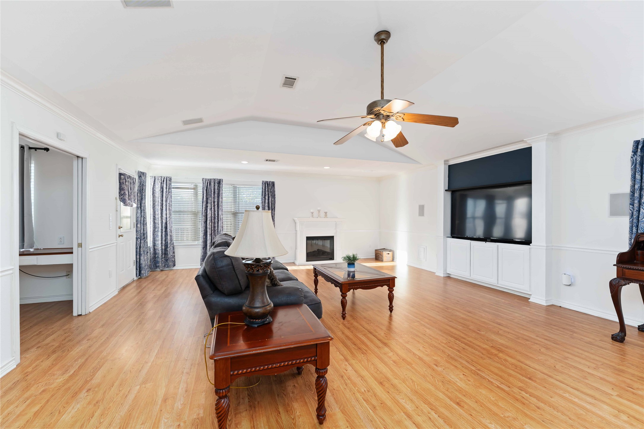 606 Packer Court Webster, TX 77598 - Photo 21 of 28 This spacious living room features elegant wood flooring, a cozy fireplace, and a large built-in TV. It's bright and airy with multiple windows, complemented by stylish curtains.