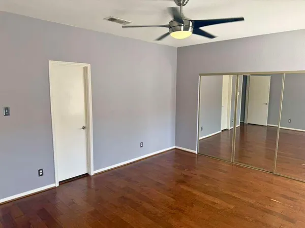 an empty room with wooden floor ceiling fan and windows