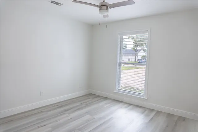 an empty room with wooden floor fan and windows