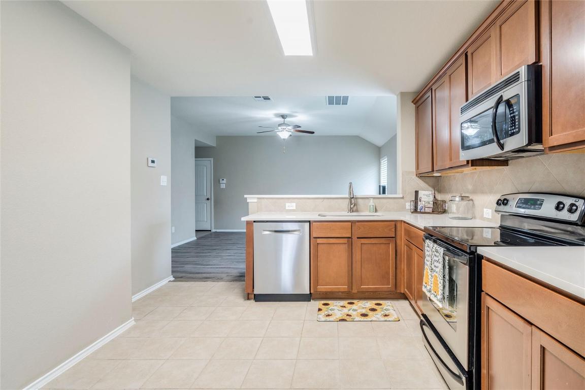 185 Housefinch Loop Leander, TX 78641 - Photo 12 of 39 Kitchen with stainless steel appliances, backsplash, a peninsula, brown cabinets, and light tile patterned floors