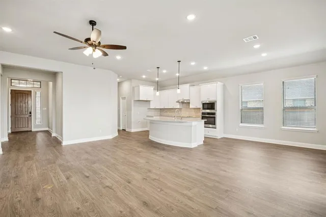 a view of an empty room with wooden floor and a kitchen
