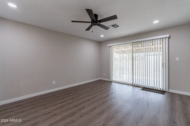an empty room with wooden floor fan and windows