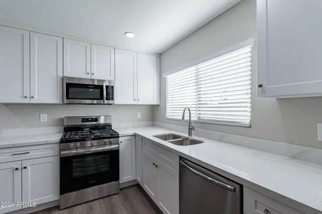 a kitchen with granite countertop white cabinets appliances a sink and a window