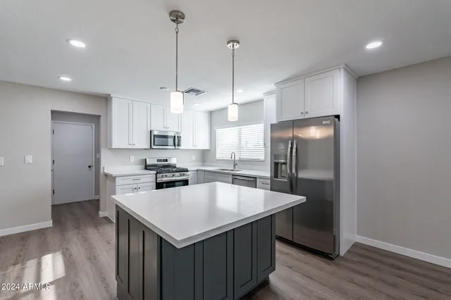 a kitchen with stainless steel appliances granite countertop a sink a stove a refrigerator a center island and wooden floor