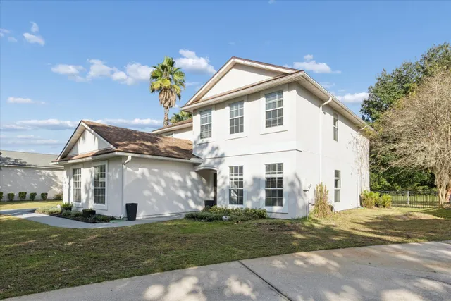 a view of a white house next to a yard with big trees