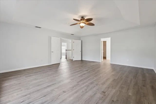 a view of an empty room with wooden floor and a ceiling fan