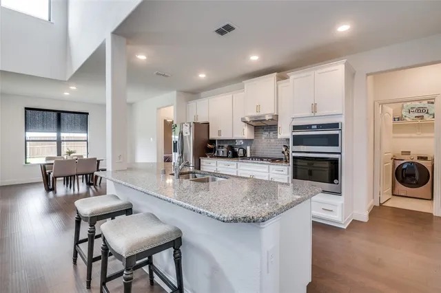 a kitchen with stainless steel appliances granite countertop a stove top oven a sink a dining table and chairs with wooden floor