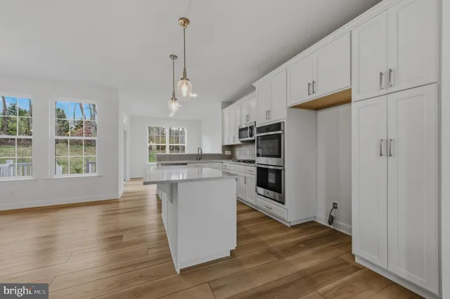 a view of kitchen with stainless steel appliances granite countertop a refrigerator a stove a sink dishwasher and white cabinets with wooden floor