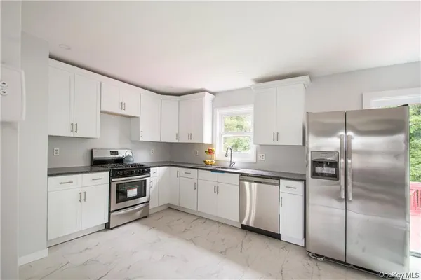 a kitchen with stainless steel appliances a refrigerator a sink a stove and white cabinets
