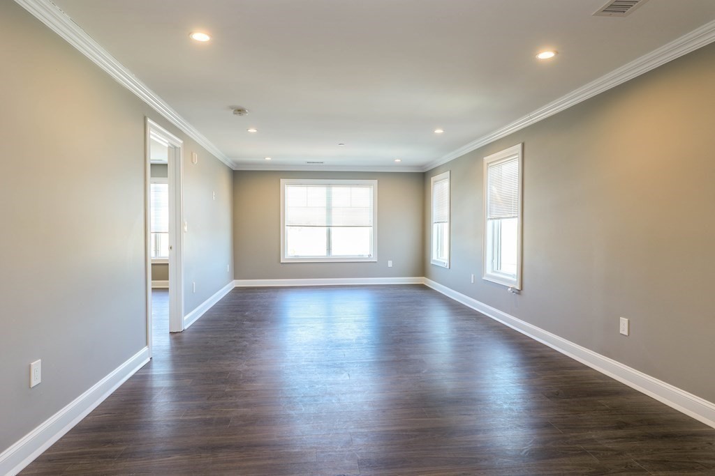918 Providence Highway, Unit 314 Dedham, MA 02026 - Photo 4 of 10 an empty room with wooden floor and windows with curtains