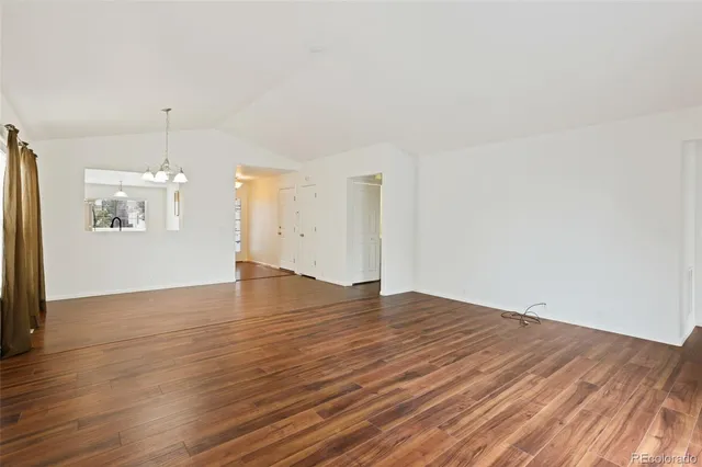an empty room with wooden floor kitchen view and a window