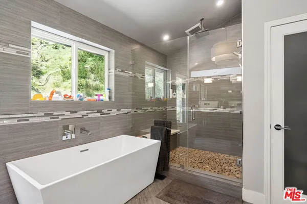 a bathroom with a tub a sink and a large mirror next to a window