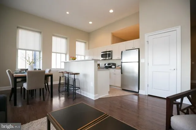 a kitchen with stainless steel appliances a dining table chairs refrigerator and sink