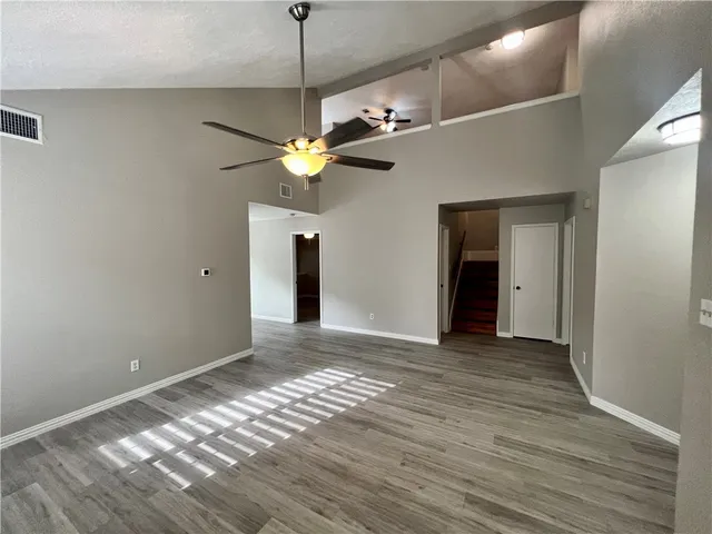 a view of an empty room with wooden floor and a ceiling fan