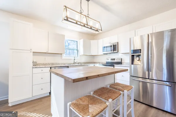 a kitchen with stainless steel appliances granite countertop a refrigerator a stove a sink dishwasher and white cabinets with wooden floor