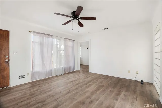 an empty room with wooden floor fan and windows