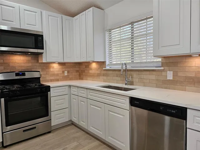 a kitchen with granite countertop white cabinets appliances a sink and a window
