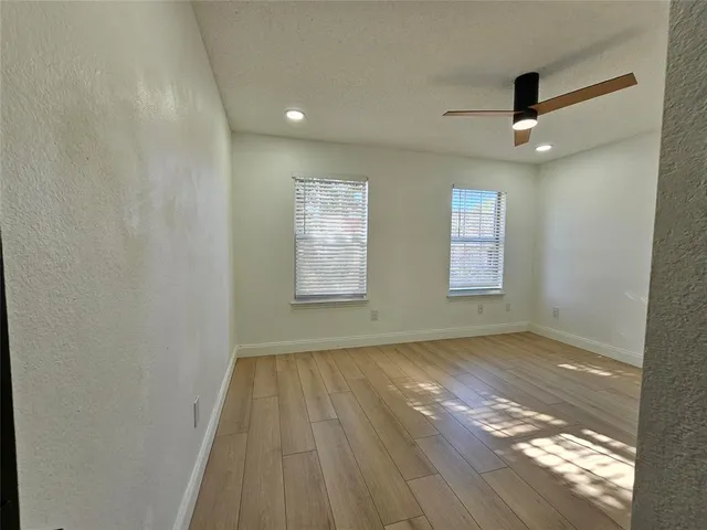 an empty room with wooden floor fan and windows