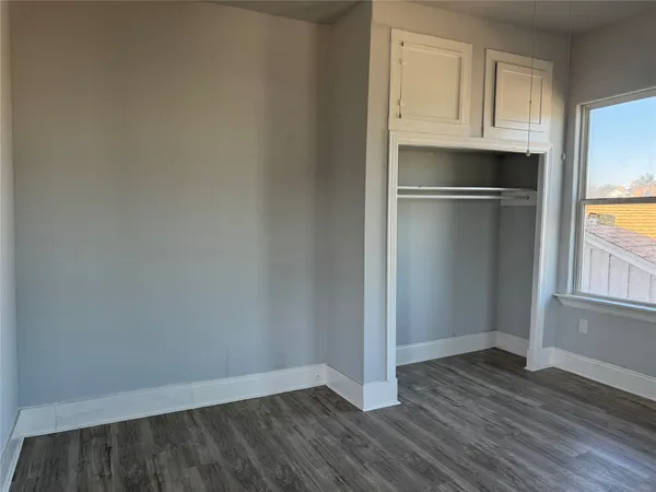 an empty room with wooden floor closet and windows