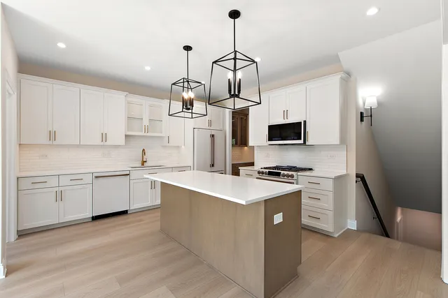 a kitchen with stainless steel appliances a stove a sink dishwasher a refrigerator and white cabinets with wooden floor