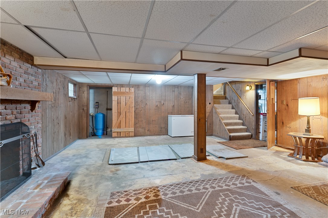 6370 Fairview Road Youngstown, OH 44515 - Photo 32 of 38 Finished basement with a fireplace, wooden walls, white refrigerator, stairs, and a water pressure tank