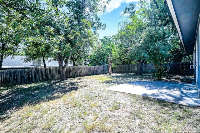a view of a backyard with large trees and wooden fence