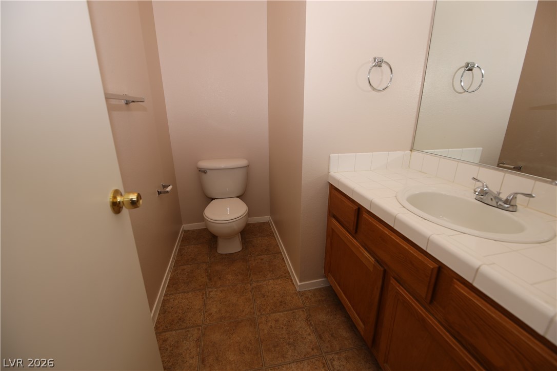 8220 Maplestar Road Las Vegas, NV 89128 - Photo 12 of 29 Functional bathroom featuring a simple vanity with a tiled counter and a compact commode.